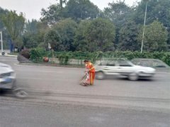 环卫工道路中央清理垃圾 多次与行驶的车辆擦肩
